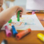 Dítě kreslí u stolu s voskovkami – ilustrační fotografie