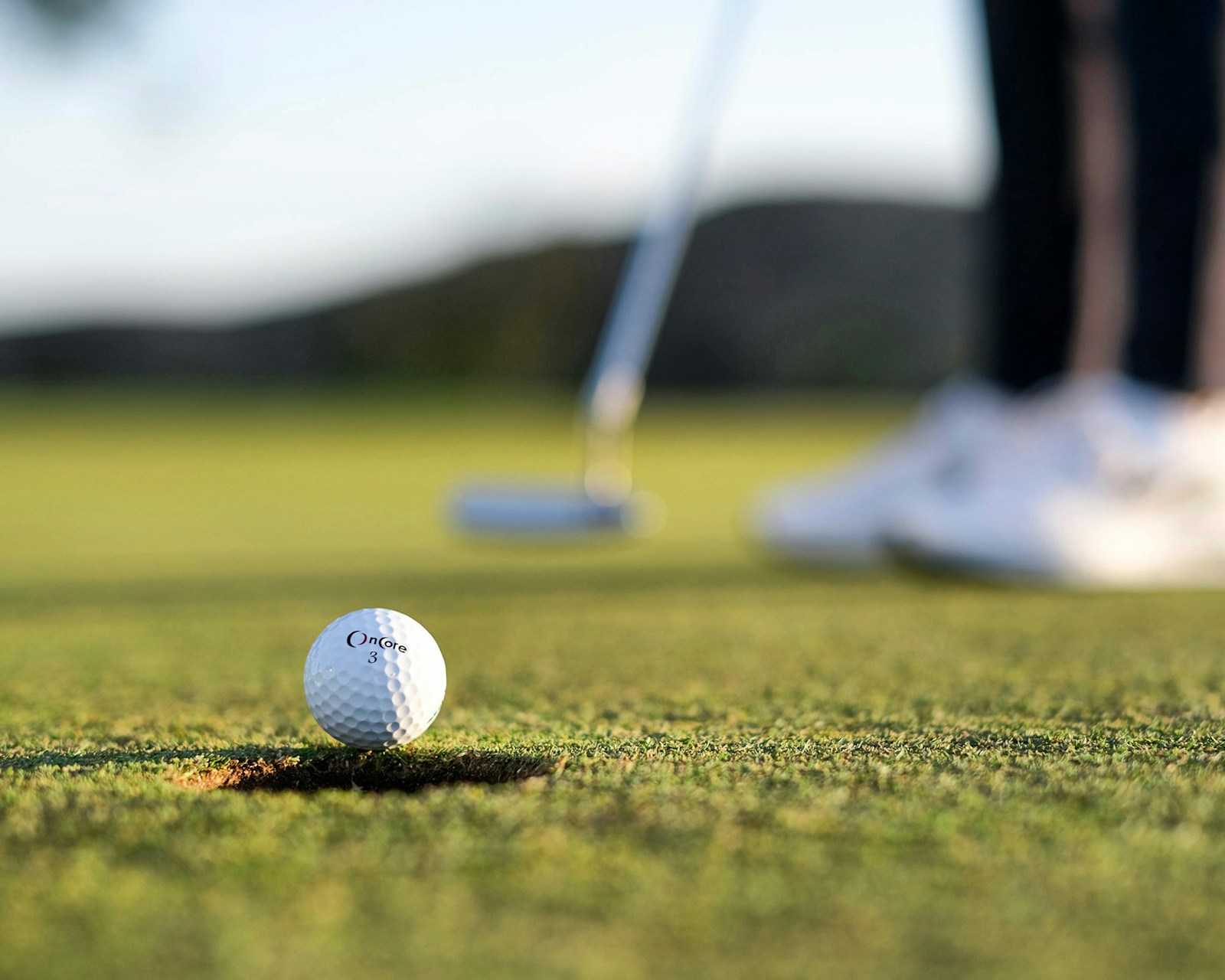 Golfový míček před hráčem a holí na trávě, ilustrační fotografie